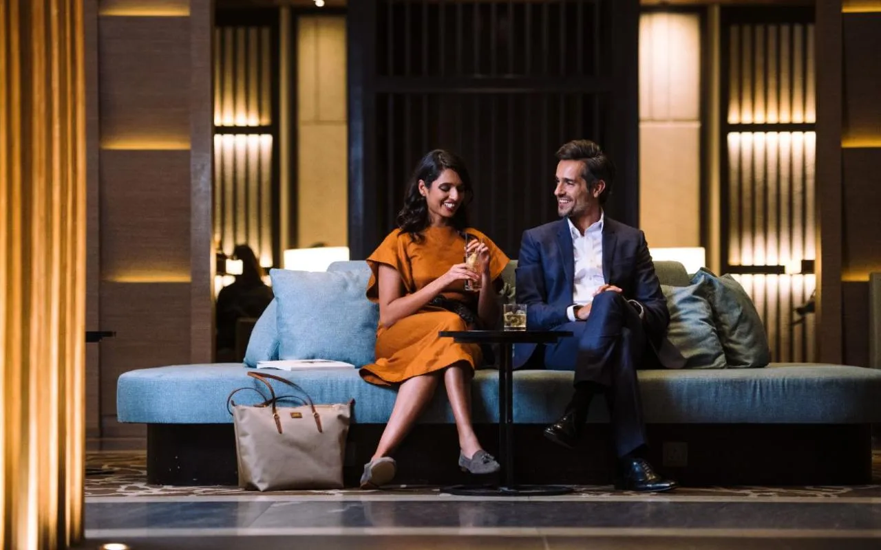 Two passengers relaxing with drinks on a sofa inside a Heathrow Airport lounge
