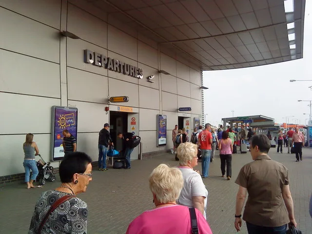 Departures entrance at Luton Airport terminal with passengers and luggage trolleys outside