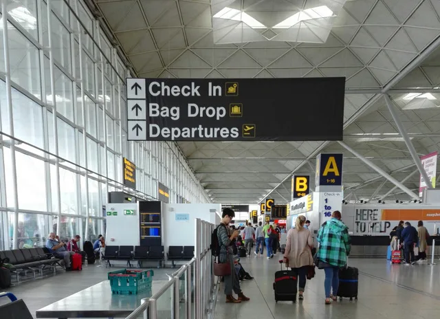 Stansted Airport departures concourse with Check In, Bag Drop and Departures signage and passengers with luggage